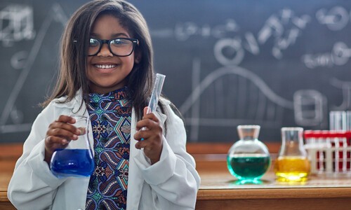 little girl in white lab coat holding glass container with blue liquid