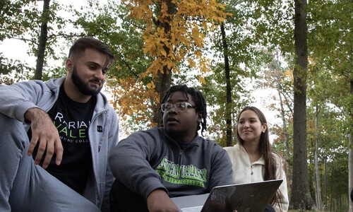 three students outside with middle student holding laptop