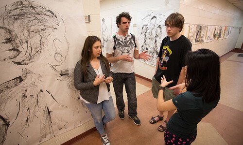 four students next to murals in arts building