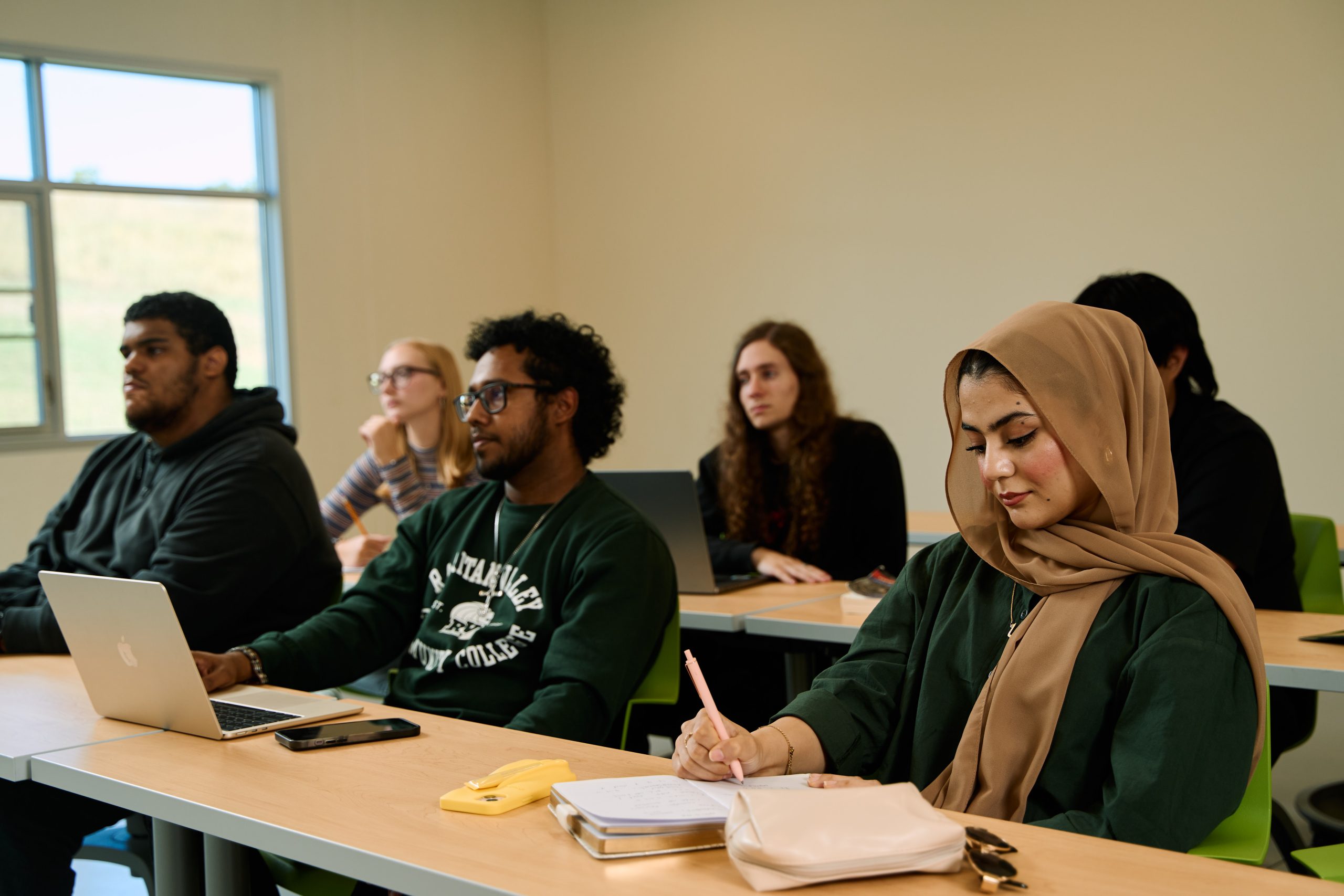 Classroom full of students sitting at tables, looking forward or looking down writting