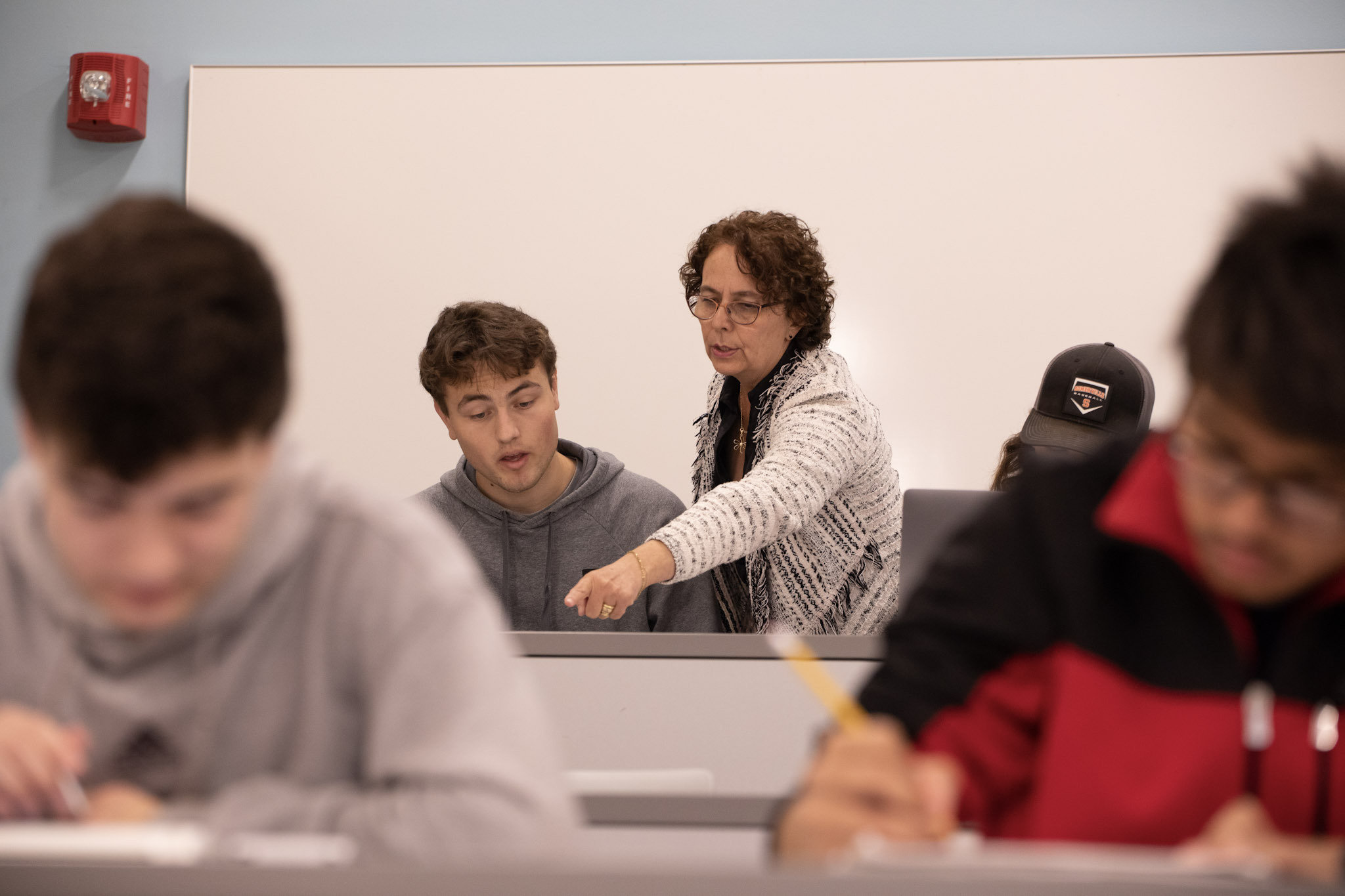 teacher pointing over a student's shoulder assisting with assignment