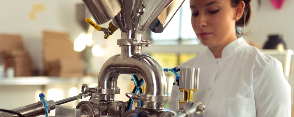 A student in a laboratory setting operates stainless steel biomanufacturing equipment as part of a Good Manufacturing Practices (GMP) certification training program.