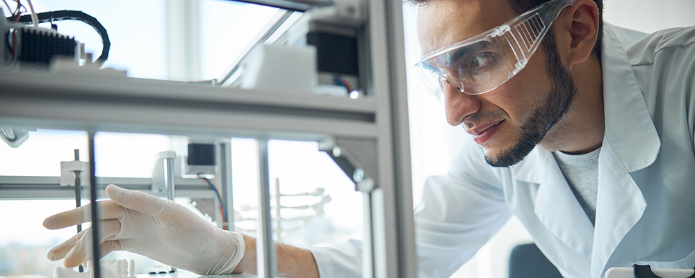 A scientist wearing protective goggles, gloves, and a lab coat carefully adjusts equipment inside a clean laboratory environment, highlighting precision and safety in pharmaceutical aseptic manufacturing.