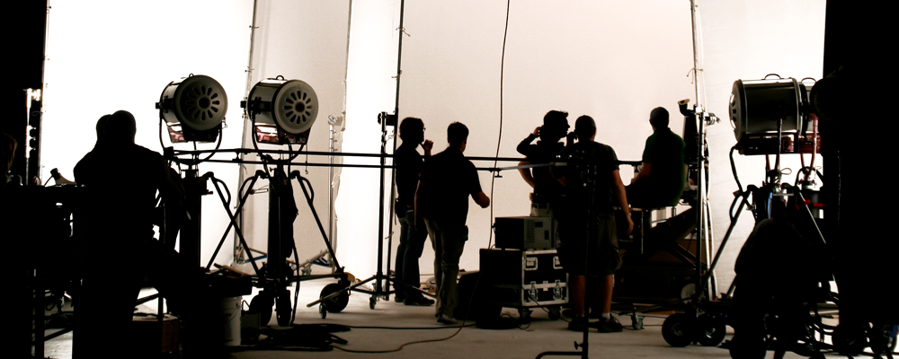 silloutte image of a busy film set with multiple people and light equipment