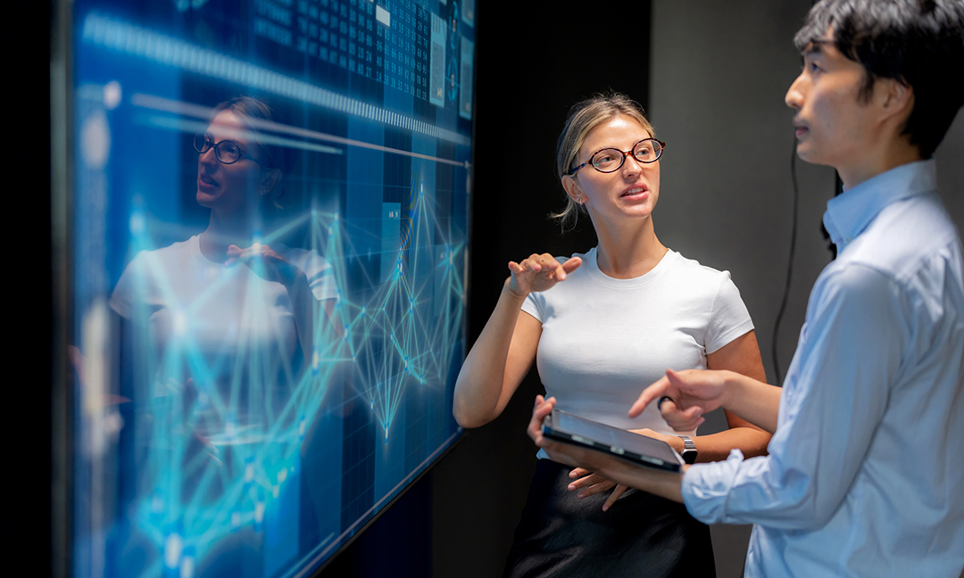 Business meeting in modern office with female programmer explaining infographic on screen to Japanese manager. Teamwork, strategy, innovation, coding, big data, AI, and technology presentation for success.
