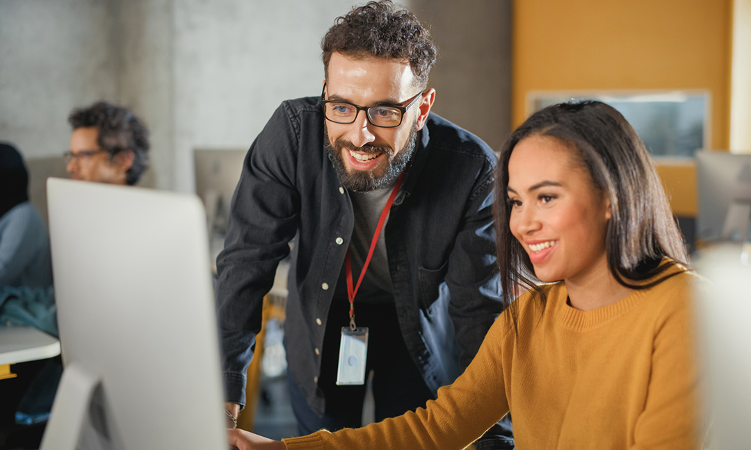 Man teaching a women on a computer, smiling focused on computer screen