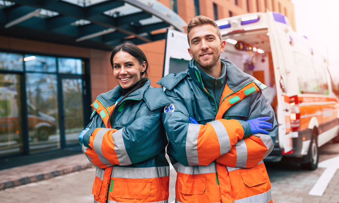 Two confident young doctors looking on the camera on ambulance and hospital background