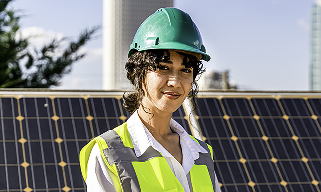 Woman standing in front of solar panels wearing a green hard hat