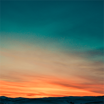 A peaceful sunset casts warm orange and gold hues across the horizon, illuminating a calm landscape of rolling hills beneath a softly fading evening sky.