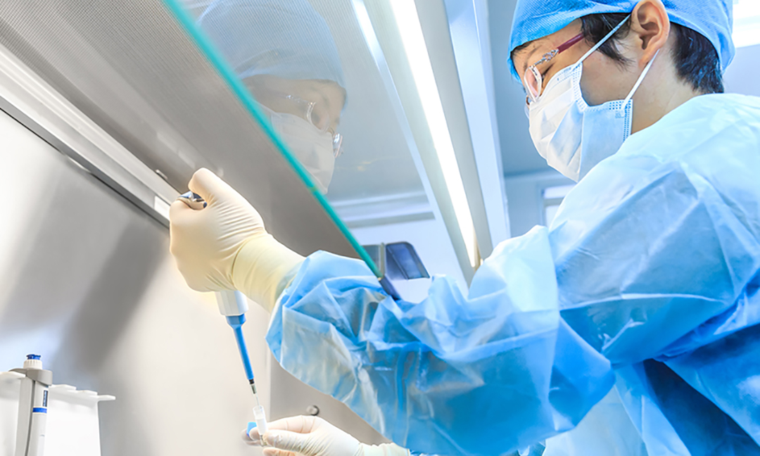 technician in full clean environment dress filling container with pipet