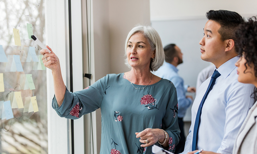 Diverse group of professionals working together, using a glass wall with notes for brainstorming and sharing ideas in an office.