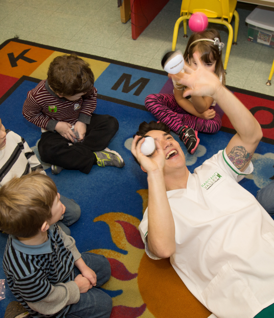 Image of a Children's Campus employee juggling with young children watching.