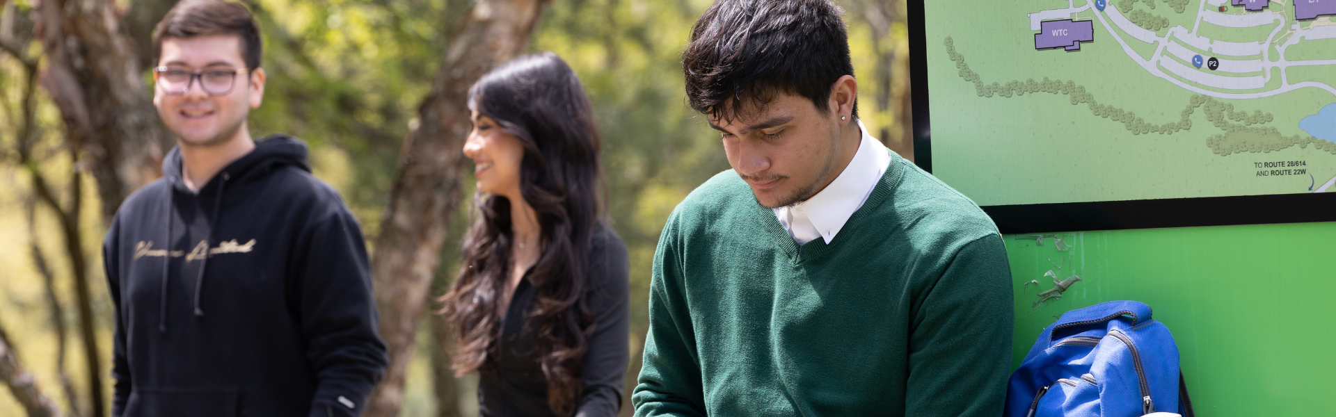 Image of a student reading a book outside, while other students walk by.