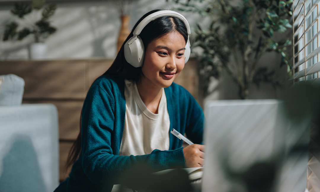 Woman enjoying her online class, attentively taking notes as she stays engaged and focused. With a sense of curiosity and dedication, she embraces the opportunity to learn from home and improve her knowledge