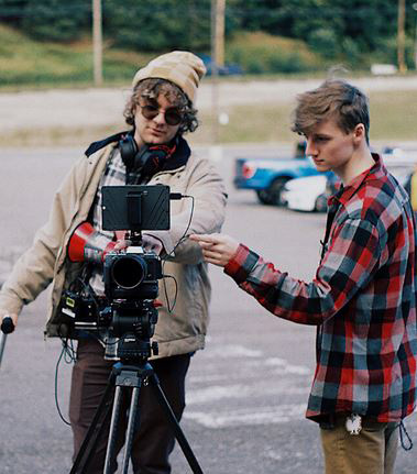 two men working outside with a movie camera focused forward, cold weather clothing.