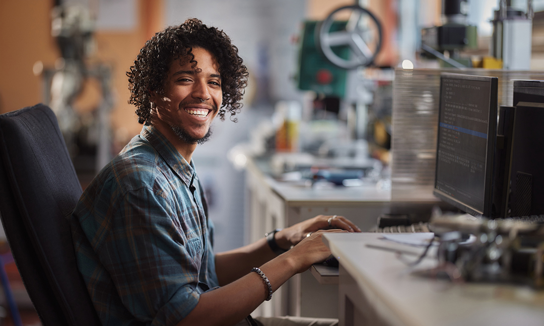 Happy African American male programmer working on desktop PC in a lab and looking at camera.