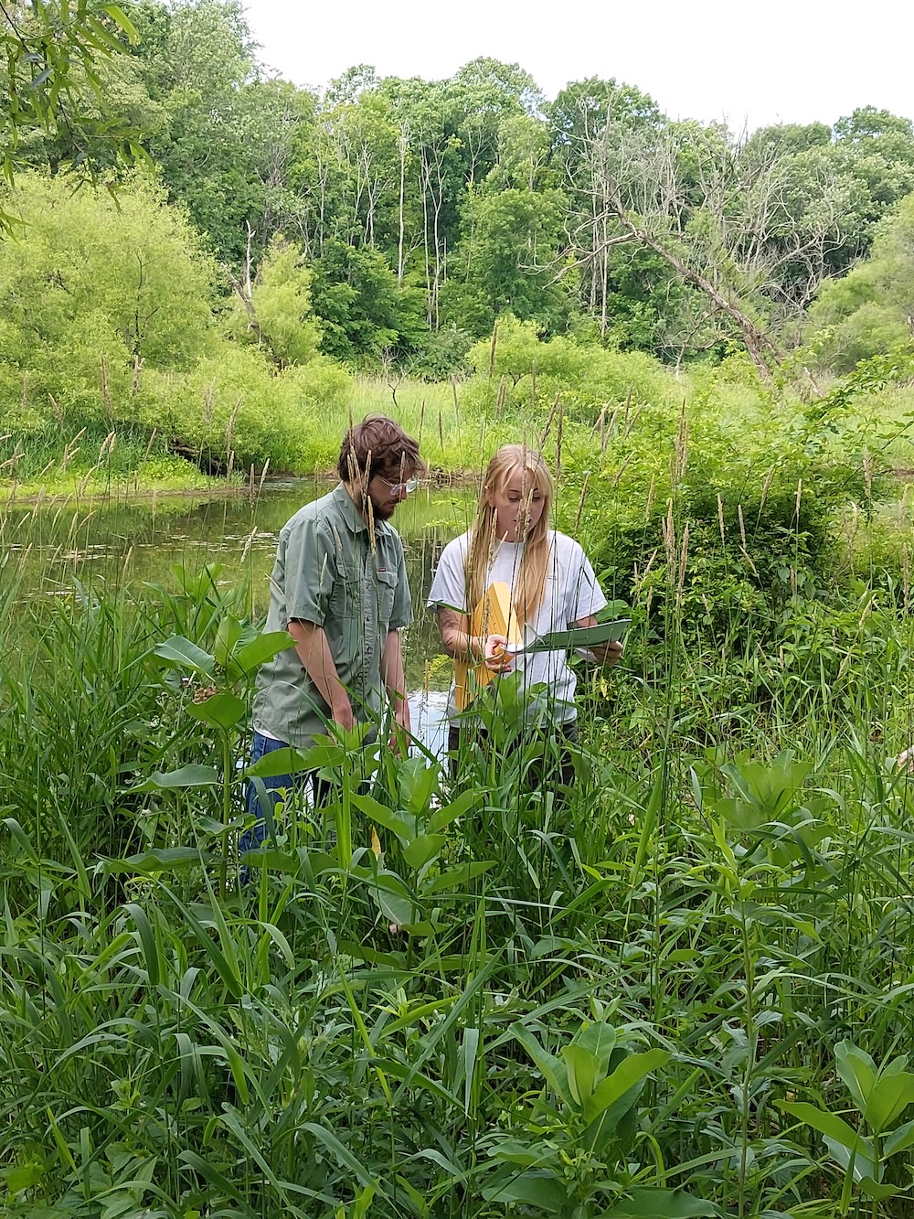 two students taking notes in tall grass