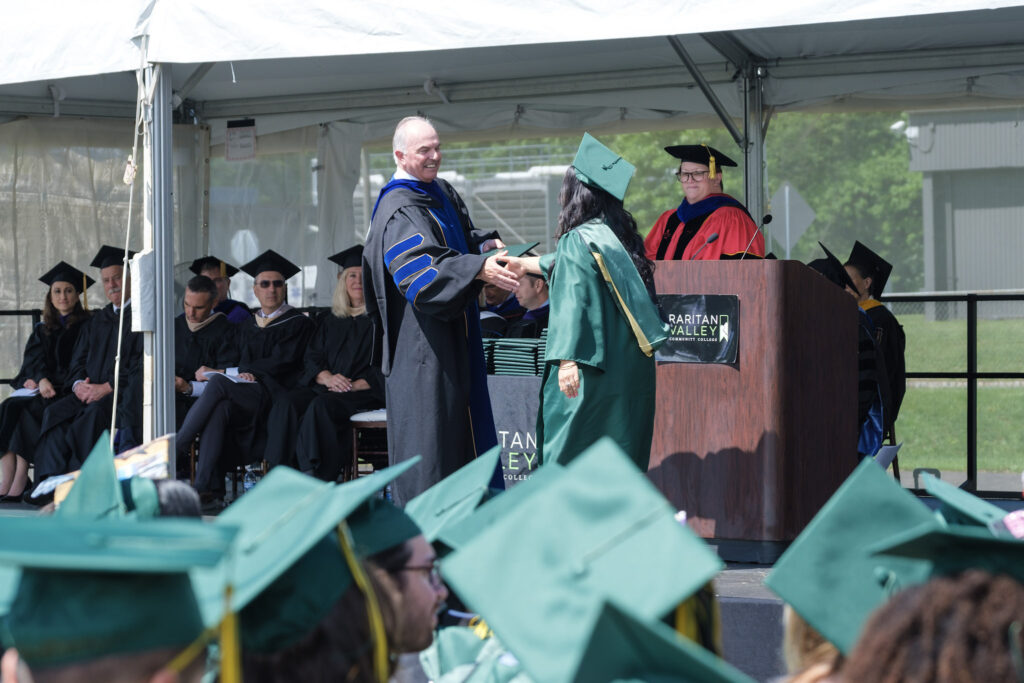RVCC graduate receives a diploma on stage during Commencement as faculty and fellow graduates look on.