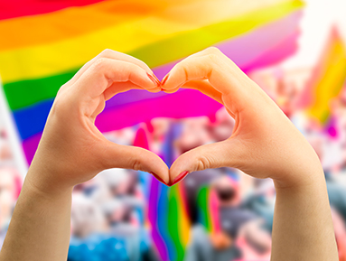 heart hands in front of crowd waving flags with multicolor stripes