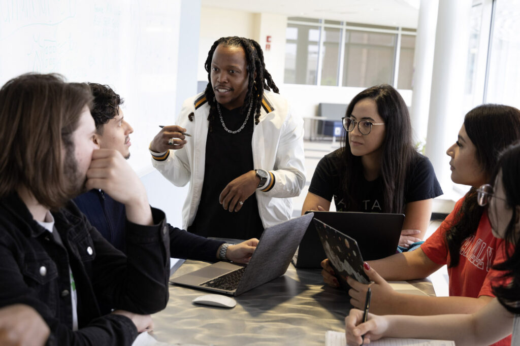 students around table with one standing wearing white jacket