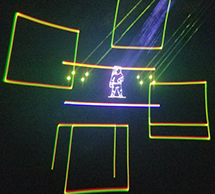 Colorful laser outlines form geometric shapes around a small illuminated figure against a dark background.